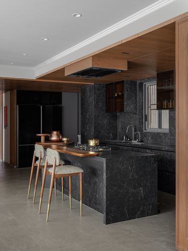 Dark stone kitchen island with wood-clad ceiling and stool seating in modern home