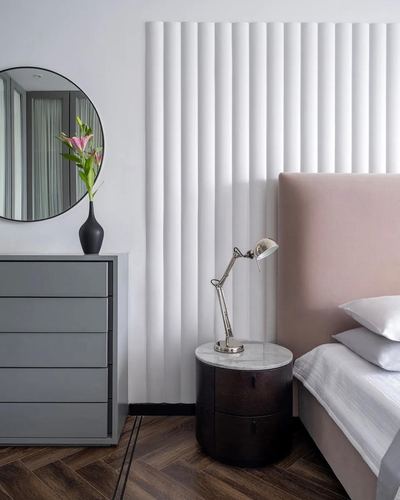 Bedroom corner with fluted white wall, blush headboard, round marble-top nightstand and grey dresser