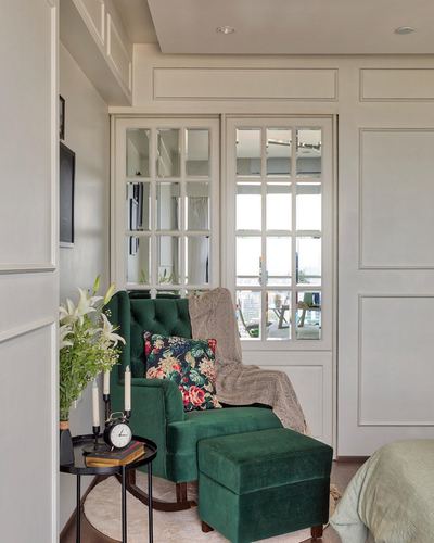 Emerald tufted wingback chair with ottoman beside mirrored french windows in a paneled bedroom corner