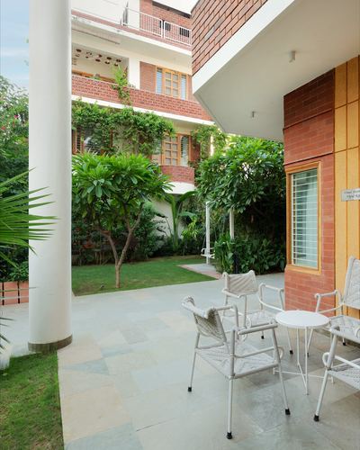 Covered terrace with woven chairs overlooking a brick building and courtyard garden in Jaipur