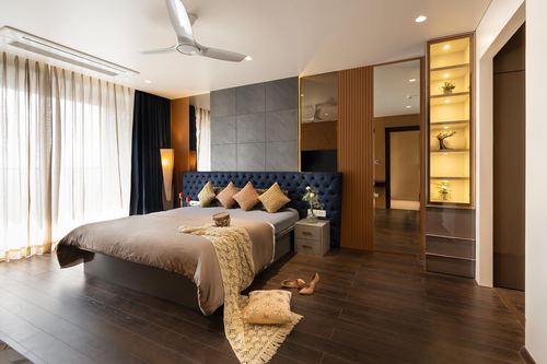 Bedroom with navy tufted headboard, dark wood floor, and backlit display shelving unit