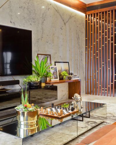 Living room with marble wall, wall-mounted tv, wooden console with plants, and mirrored coffee table with chess set