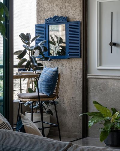 Blue shuttered mirror above rattan chair with indigo cushion on textured balcony wall