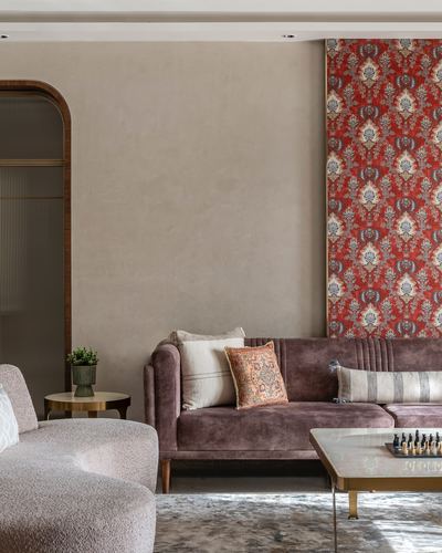 Living room with mauve velvet sofa, boucle armchair, and red patterned wall panel beside arched doorway