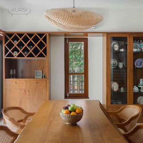 Wooden dining table with fruit bowl, cane chairs, teak cabinetry and glass-front crockery cabinet