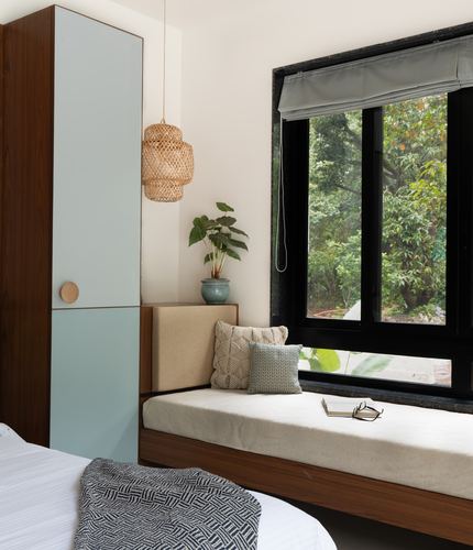 Wood-toned bedroom with window seat, rattan pendant light, and view of trees through dark-framed window.