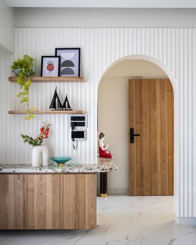 Foyer with fluted white wall, arched wooden door, terrazzo-topped wood console and open shelves