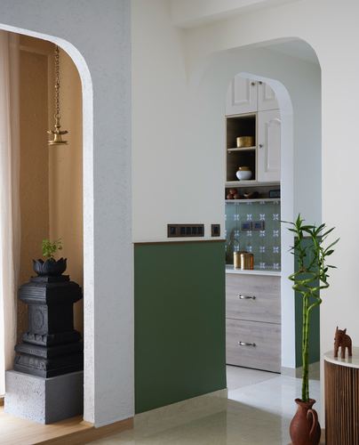 Arched pooja niche with hanging brass lamp beside olive green wall and glimpse into kitchen
