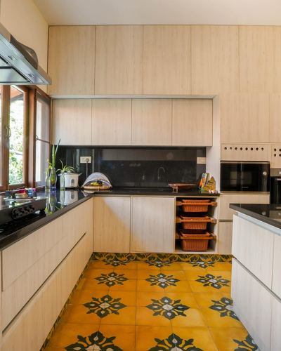 U-shaped light wood kitchen with black countertops and patterned yellow floor tiles
