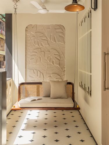 Cane and wood hanging swing seat below a carved leaf-relief niche on patterned tiled balcony floor