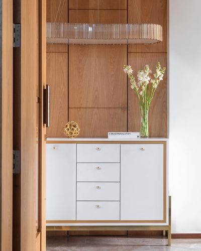 White and gold sideboard against wood-paneled wall with ring chandelier and flowers