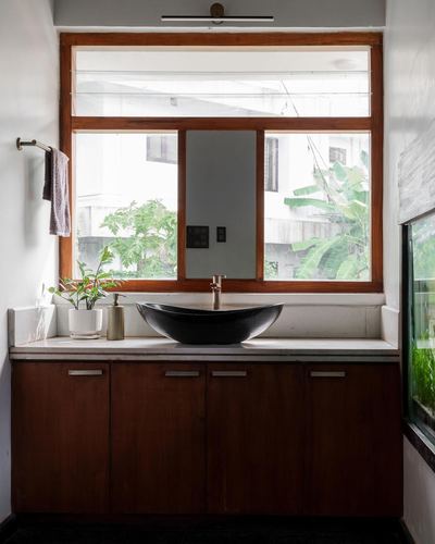 Bathroom vanity with black boat-shaped sink under wood-framed window with mirror insert
