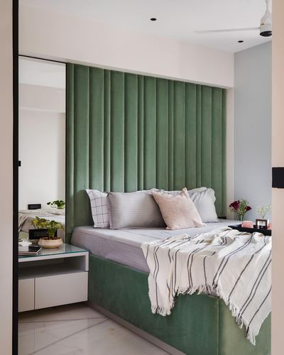 Bedroom with fluted green velvet headboard wall, white bedding, striped throw and marble flooring