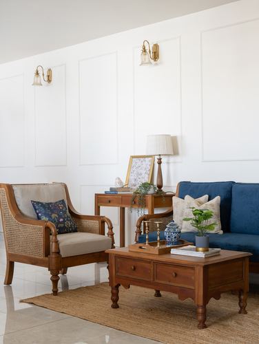 Living room corner with cane armchair, navy sofa, wooden coffee table and paneled wall