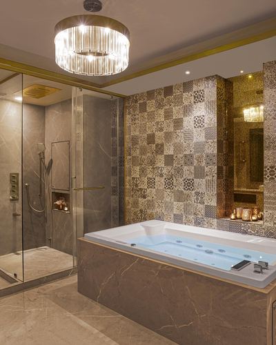 Luxury bathroom with jacuzzi tub, patterned tile accent wall, and crystal drum chandelier
