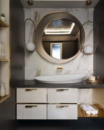 Bathroom vanity with round brass mirror, marble backsplash, and fluted white cabinetry