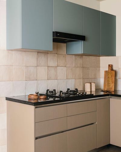 L-shaped kitchen with sage green upper cabinets, black hob, and cream tiled backsplash
