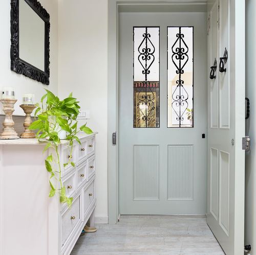 Foyer with white dresser, pothos plant, ornate black mirror, and sage-green paneled door with iron grillework