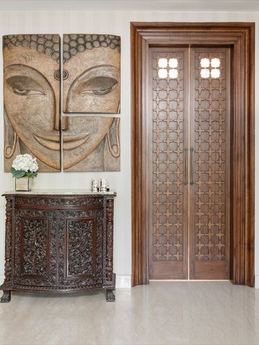 Carved wooden double doors with lattice pattern beside an antique carved console and Buddha wall art
