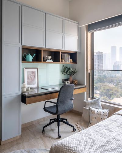 Built-in study desk with grey cabinetry, open shelving, and city view beside a bedroom window