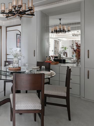 Dining area with round glass table, dark wood chairs, and mirrored cabinetry reflecting a chandelier.
