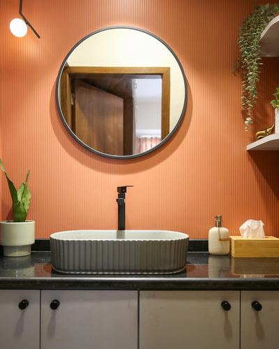 Terracotta ribbed bathroom wall with round mirror over ribbed ceramic sink and black countertop