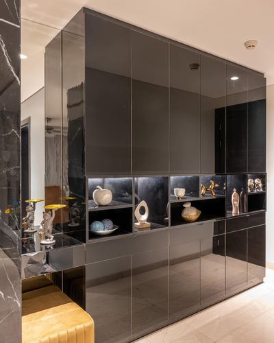 Glossy dark storage wall with backlit display niches holding decorative objects in a marble-floored foyer