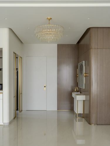 Entry foyer with crystal chandelier, curved wood-clad wall, and brass-legged console table