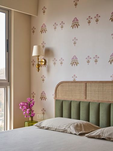 Bed with green channel headboard and cane arch against floral wallpapered wall, brass sconce, window light