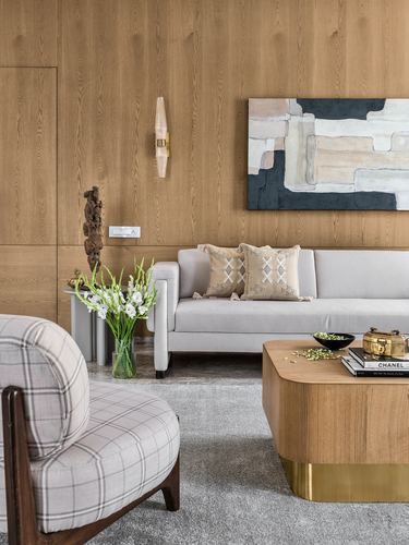 Living room with wood-panelled wall, grey sofa, plaid armchair, and brass-based coffee table
