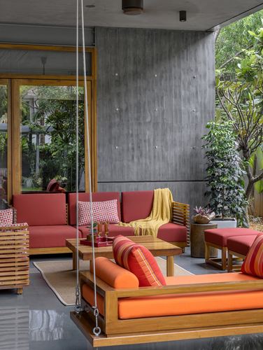 Covered patio with red slatted sofa, orange wooden swing, and concrete wall against greenery