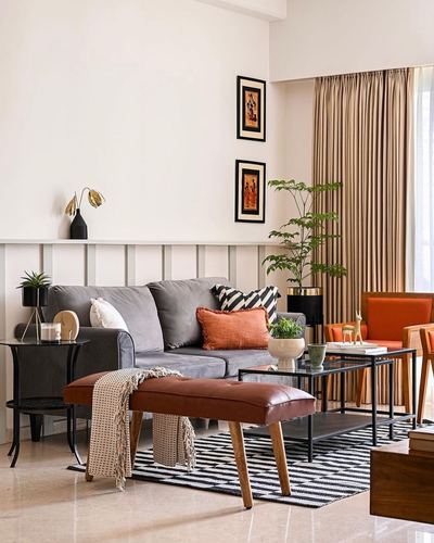 Living room with grey sofa, orange cushions, leather bench, and striped rug under warm light