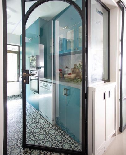 Teal glossy kitchen seen through an arched black-framed glass door with patterned cement tile floor