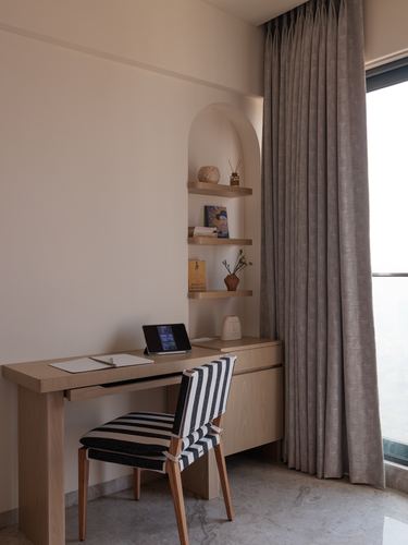 Wooden desk with tablet beneath an arched niche shelf, striped chair, beige curtain by window