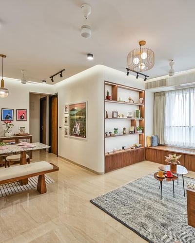 Open-plan living and dining space with curved wood shelving wall and window seat in Mumbai apartment