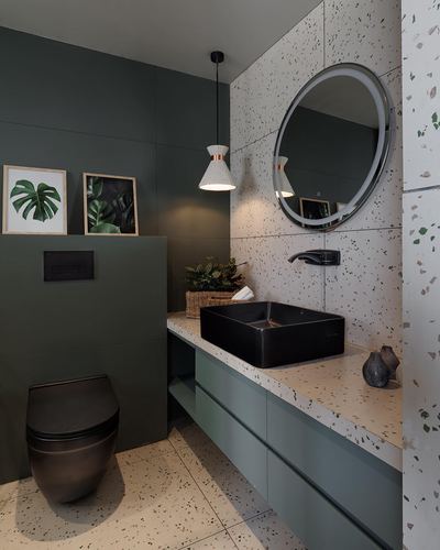 Dark green bathroom with terrazzo counter, black matte sink and toilet, round backlit mirror