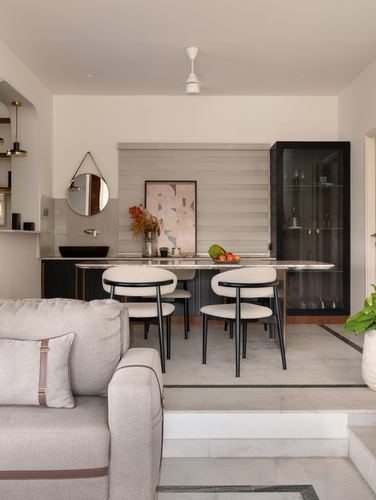 Dining nook with round table, white curved chairs, black display cabinet and round mirror above sink counter