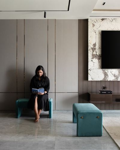 Woman reading on teal bench in grey-paneled living room with marble-clad tv wall