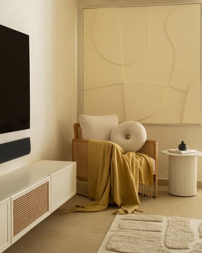 Cane armchair with mustard throw beside fluted side table under a textured beige wall panel