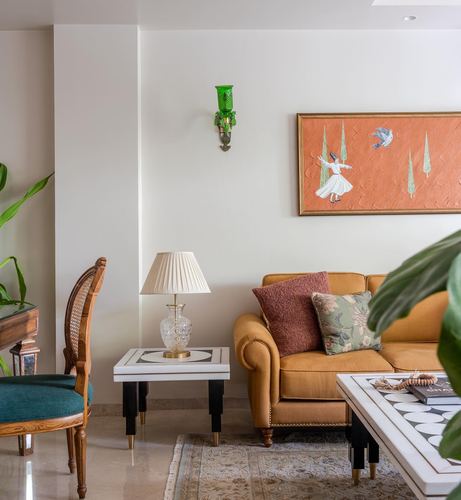 Living room corner with mustard sofa, marble side tables, cane chair, and framed dance painting