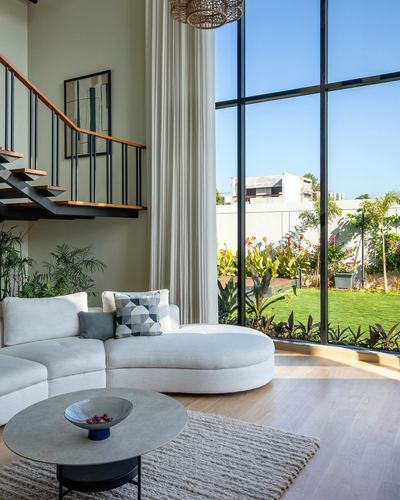 Curved white sofa in double-height living room with floating staircase and floor-to-ceiling windows overlooking garden
