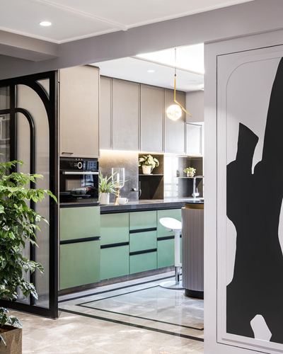 Modern kitchen with sage green lower cabinets, beige uppers, black countertop, and reeded glass partition
