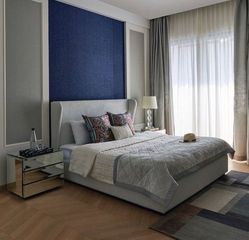Bedroom with grey wingback bed, navy textured headboard wall, mirrored nightstand and sheer curtains