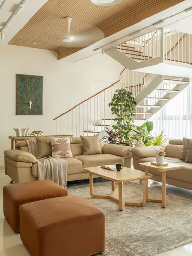 Living room with tan sofas, leather ottomans, wooden coffee tables, and open staircase behind
