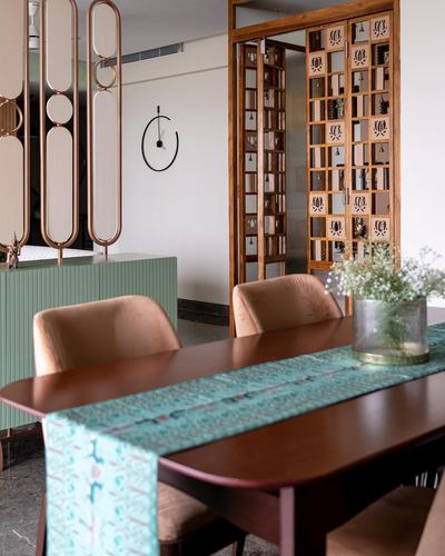 Dining table with teal runner, velvet chairs, and a carved wooden lattice partition beyond
