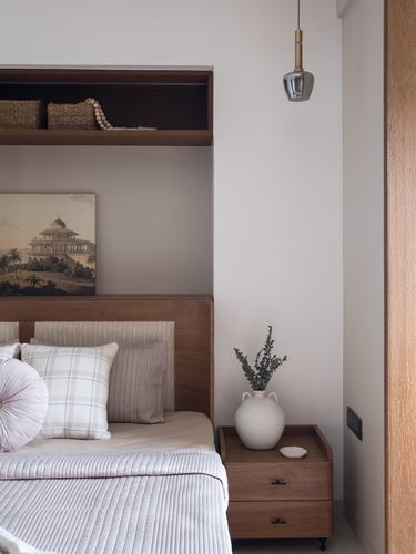 Bedroom corner with wood headboard, open shelf niche, pendant light, and nightstand with vase