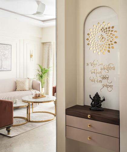 Arched pooja niche with gold om motif and ganesha idol beside blush drawer unit, living room visible left