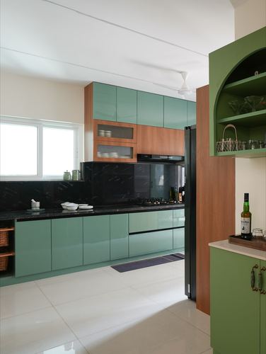 Glossy green kitchen cabinetry with wood accents and a dark stone backsplash beside an arched display niche