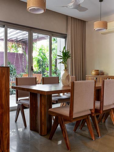 Wooden dining table with pink upholstered chairs beside glass doors opening to a green courtyard