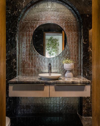 Round mirror over floating vanity in arched tiled niche with dark marble surround